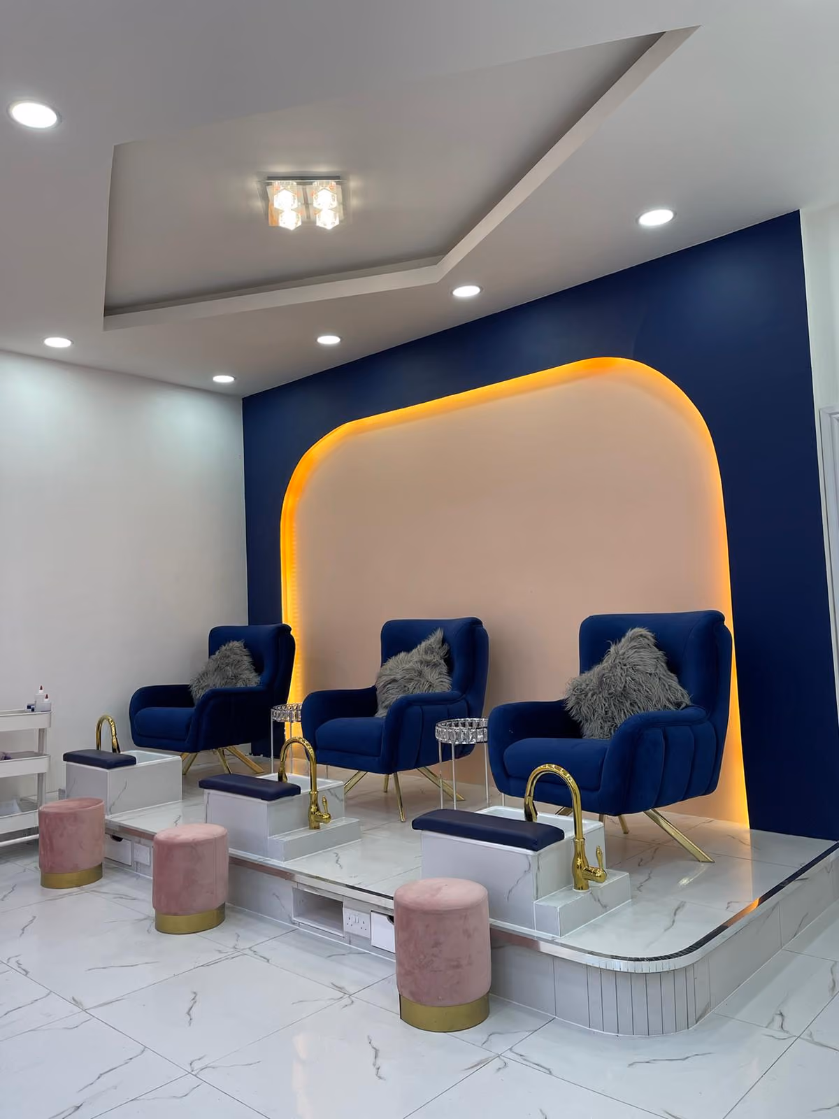 Blue velvet pedicure chairs under a lit pink arch at Vanity Nail Bar